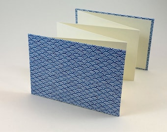 May include: A blue and white patterned paper bound book with a decorative edge. The book is folded open to reveal blank pages.