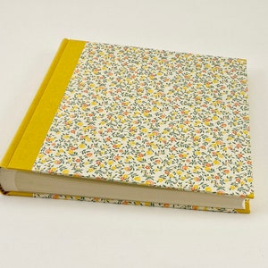 Puede incluir: Un &aacute;lbum de fotos amarillo con una cubierta de patr&oacute;n floral. El &aacute;lbum tiene una columna vertebral amarilla y est&aacute; cerrado.