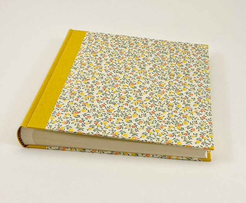 Puede incluir: Un &aacute;lbum de fotos amarillo con una cubierta de patr&oacute;n floral. El &aacute;lbum tiene una columna vertebral amarilla y est&aacute; cerrado.