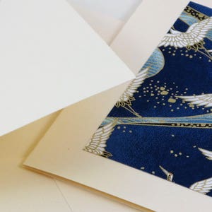 May include: A cream-colored card with a blue and gold patterned insert featuring white cranes flying against a dark blue background. The pattern includes gold dots and lines.