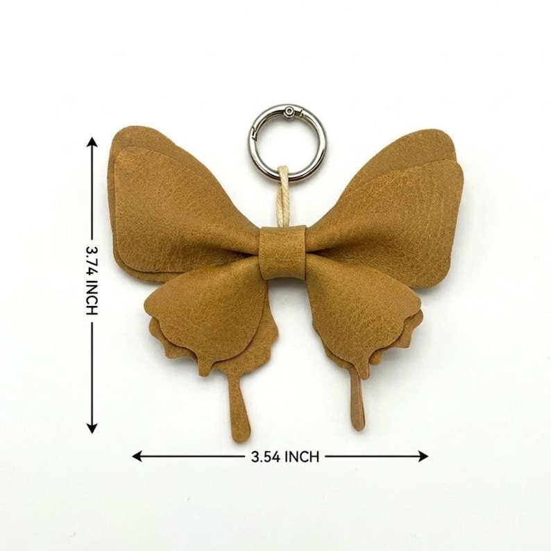 May include: A tan butterfly-shaped keyring made of layered material with a silver metal ring. The item measures 9.5 cm in height and 9.0 cm in width, as indicated by the black arrows and text labels on the image.