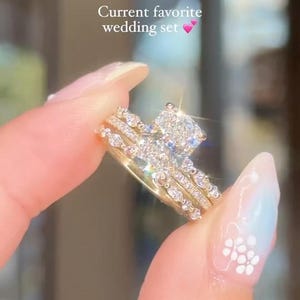 May include: A gold wedding ring set consisting of three stacked bands with clear, sparkling stones. The central ring features a prominent rectangular stone, while the flanking bands are adorned with smaller, round and marquise-cut stones. Text reads: Current favorite wedding set.