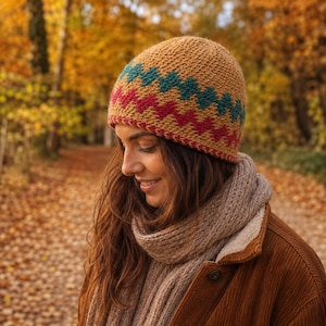 Puede incluir: Un gorro de punto color amarillo mostaza con dos franjas horizontales en zigzag de color verde azulado y rosa oscuro. El gorro tiene una apariencia tejida y texturizada con una forma redondeada. El diseño presenta un patrón geométrico.