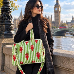 May include: A rectangular quilted laptop bag featuring a repeating pattern of red lobsters on a white and light green vertical striped background, equipped with two top handles and a detachable shoulder strap with matching lobster print.