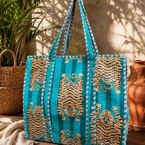 Peut inclure: Un sac fourre-tout matelassé de couleur bleu sarcelle vif avec un motif répétitif de tigres noirs et dorés. Le sac possède deux longues anses avec une bordure rayée assortie au passepoil qui souligne les bords du corps rectangulaire.