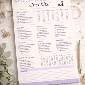 May include: ADHD Cleaning Checklist notepad with a spiral binding. The checklist includes daily, weekly, and monthly chores. A cup of coffee, pens, and decorative items are arranged around the notepad.