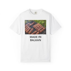 May include: White t-shirt with a graphic of grilled meat on a grill. The image is above the text "MADE IN BALKAN" in black, bold letters. The shirt is a casual, everyday wear item.