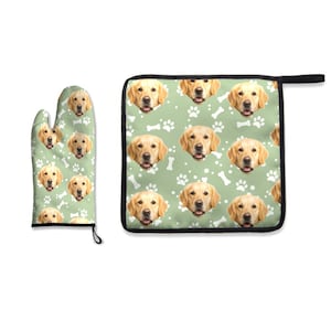 May include: A kitchen oven mitt and a square pot holder featuring a repeating pattern of golden retriever dog faces, white paw prints, and white bone shapes on a light sage green background, finished with black trim and a hanging loop.