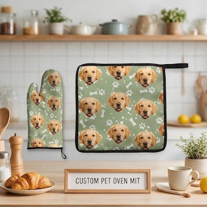 Könnte beinhalten: Ein salbeigrüner Ofenhandschuh und ein quadratischer Topflappen mit einem sich wiederholenden Muster aus Golden Retriever-Gesichtern, weißen Pfotenabdrücken und weißen Knochen. Ein Holzschild zeigt den Text CUSTOM PET OVEN MIT.