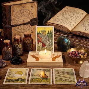 Puede incluir: Un portavelas de madera con una vela de té, con una ilustración de dos manos, rodeado de cartas del tarot, dos frascos de vidrio con hierbas secas, un libro abierto con diagramas astrológicos, una piedra oscura y un cuenco con pétalos secos.