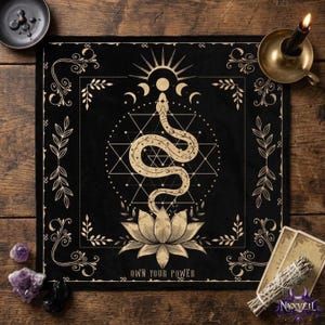 May include: A square black altar cloth featuring a gold-coloured print of a snake coiled above a lotus flower, centred within a geometric star pattern. Above the snake are moon phases and a sunburst. The text "OWN YOUR POWER" is printed at the bottom.