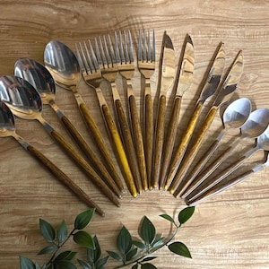 May include: A set of stainless steel flatware featuring brown wood-grain patterned handles. The collection includes four large spoons, three forks, four knives, and three small spoons, all arranged in a fan shape with polished metal heads.