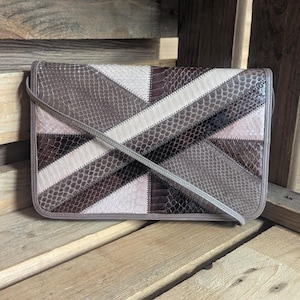 May include: A rectangular clutch bag featuring a geometric patchwork design made of textured faux snakeskin material in shades of brown, beige, cream, and dark grey, with a thin shoulder strap and a fold-over flap closure with stitched edges.