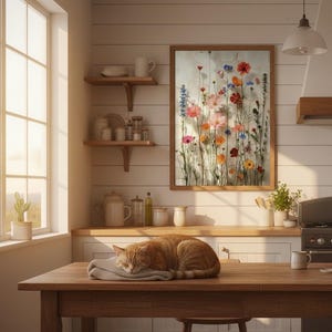 Rustikaler Landhaus-Kunstdruck in einer Küche mit weißen Holzpaneelen. Eine schlafende Katze liegt auf einem Holztisch bei warmem Sonnenuntergangslicht. Heimelige, ländliche Küchen-Dekoration.