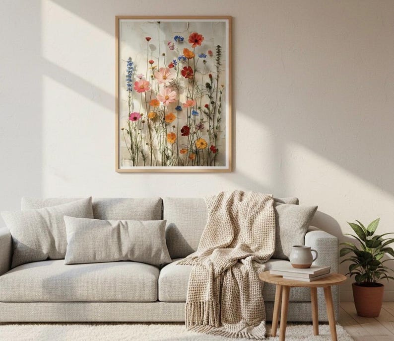 Hochwertiger botanischer Kunstdruck, hängend über einem gemütlichen beigen Sofa im Hygge-Stil. Helles Wohnzimmer mit Strickdecke, Holztisch und warmem Licht. Ästhetische Wandkunst für ein behagliches Zuhause.