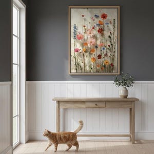 Large 20x28 framed wildflower art print on a dark gray wall with white wainscoting in a modern farmhouse hallway. A ginger cat walks across the light wooden floor, adding a touch of warmth. Features a rustic console table with a ceramic vase, perfect botanical wall decor for a welcoming entryway.
