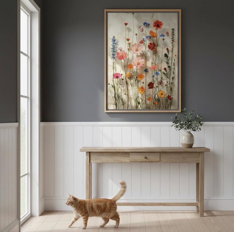 Large 20x28 framed wildflower art print on a dark gray wall with white wainscoting in a modern farmhouse hallway. A ginger cat walks across the light wooden floor, adding a touch of warmth. Features a rustic console table with a ceramic vase, perfect botanical wall decor for a welcoming entryway.