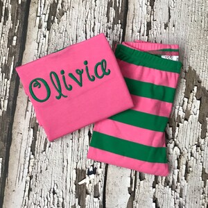May include: Pink and green striped pajamas with the name Olivia embroidered on the pink top.