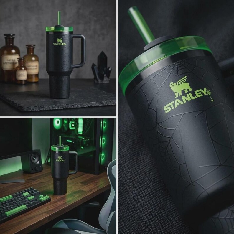 May include: Black Stanley tumbler with a green lid and straw. The tumbler has a handle and the Stanley logo in green. The design includes a spiderweb pattern and a green accent. The tumbler is shown in different settings, including a desk and a dark background.