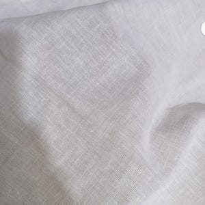Pode incluir: Uma pe&ccedil;a de tecido branco com uma textura tecida vis&iacute;vel. O material apresenta um padr&atilde;o de trama cruzada distinto criado pelo entrela&ccedil;amento de fios horizontais e verticais, resultando numa apar&ecirc;ncia semitransparente com dobras e vincos naturais.