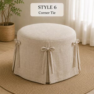 May include: A round beige ottoman with a textured fabric cover featuring a skirted base and decorative corner ties. The text STYLE 6 Corner Tie is visible above the ottoman. The piece has a flat top and a structured, cylindrical shape.