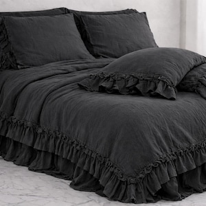 May include: A charcoal grey bed set featuring a ruffled duvet cover, pillowcases, and a bed skirt. The bedding has a textured look, and the ruffles provide a decorative touch. The set is designed for a double, king or super king-sized bed.