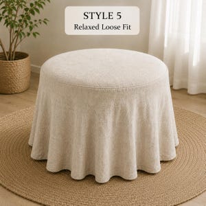 Pode incluir: Um pufe redondo com uma capa de tecido bege texturizado que apresenta um ajuste solto e relaxado com pregas franzidas ao redor da base. Acima do pufe, uma etiqueta retangular exibe o texto STYLE 5 Relaxed Loose Fit em fonte preta.