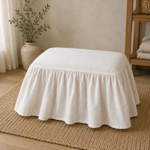 May include: A rectangular ottoman featuring a cream-coloured fabric cover with a gathered, floor-length skirt. The upholstery has a visible woven texture, and the skirt drapes evenly around all sides, creating a soft, layered appearance.