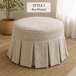 Pode incluir: Um pufe redondo estofado em tecido texturizado bege claro com uma saia de pregas tipo caixa. Uma etiqueta retangular acima do pufe exibe o texto STYLE 1 Box Pleated em fonte preta. O pufe possui um topo plano e uma base estruturada.