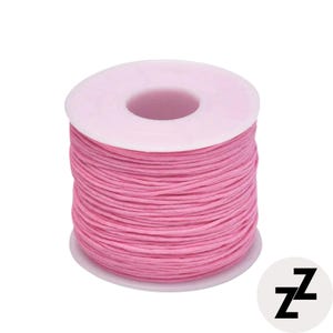 May include: A spool of pink thread, tightly wound around a white plastic core. The thread is a vibrant, solid color, and the spool is set against a plain white background. The image also includes a small, circular logo with the letter "z".