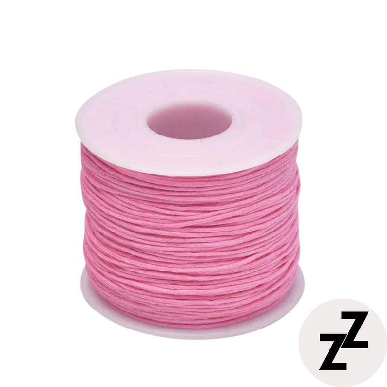 May include: A spool of pink thread, tightly wound around a white plastic core. The thread is a vibrant, solid color, and the spool is set against a plain white background. The image also includes a small, circular logo with the letter "z".