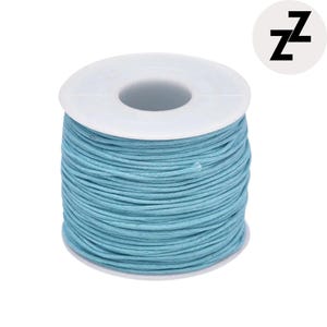 May include: A spool of light blue waxed cotton cord. The cord is tightly wound around a white plastic spool. The image includes a white circle with the black letter "z" repeated twice.