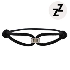 Könnte beinhalten: Schwarzes Seilarmband mit silberfarbenem Metallverschluss. Das Armband ist an jedem Ende geknotet. Ein weißer Kreis mit den schwarzen Buchstaben "ZZ" befindet sich in der oberen rechten Ecke.