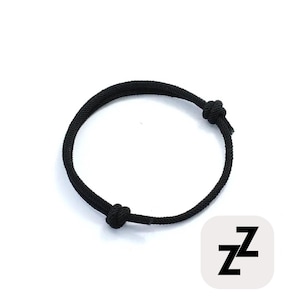 May include: Black adjustable bracelet made of a thick, woven cord. The bracelet features two knots and a sliding knot closure for a custom fit. The bracelet is shown on a white background with a small square logo with the letter "Z".