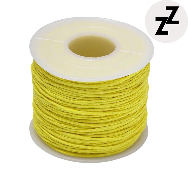 May include: A spool of bright yellow waxed thread. The thread is tightly wound around a white plastic spool. The spool has a white base and a white top with a central opening. A small, white circle with the letter "z" repeated twice is in the upper right corner.