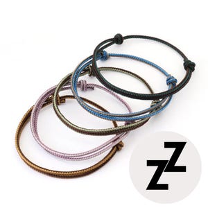 May include: Several adjustable rope bracelets in shades of brown, purple, blue, and green. Each bracelet has a sliding knot fastening. A white circle with the black letters "ZZ" is in the lower right corner.