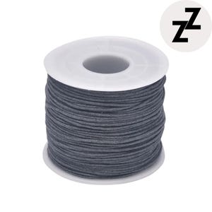 May include: A spool of dark gray waxed cord. The cord is tightly wound around a white plastic spool. A small, white circle with the black letter "Z" repeated twice is in the upper right corner.