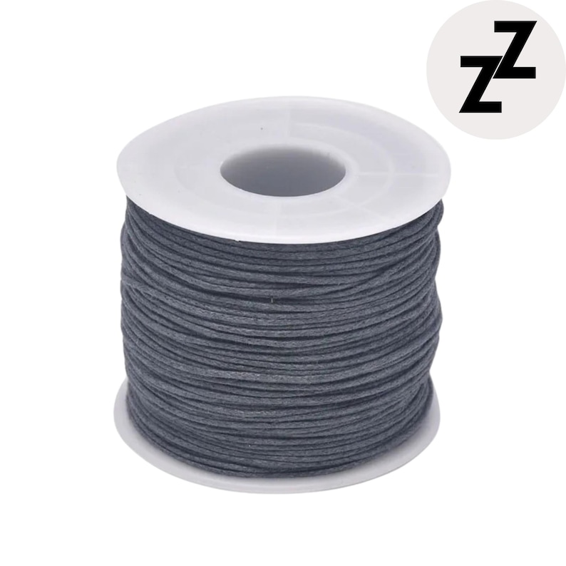 May include: A spool of dark gray waxed cord. The cord is tightly wound around a white plastic spool. A small, white circle with the black letter "Z" repeated twice is in the upper right corner.