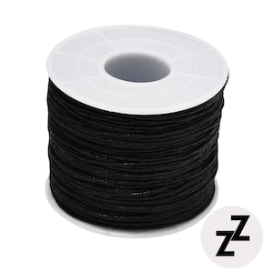 May include: A spool of black waxed cord, tightly wound around a white plastic core. The cord appears smooth and durable, suitable for various crafting projects. A white circular logo with the letters "ZZ" is in the lower right corner.