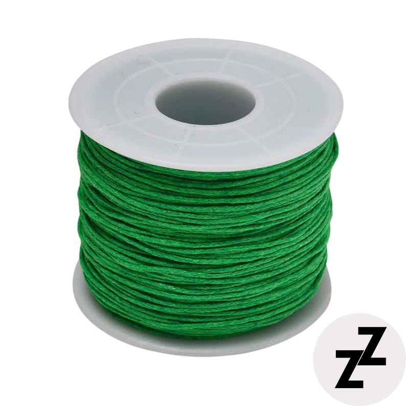 May include: A spool of bright green thread, tightly wound around a white plastic core. The thread is a vibrant, solid color, suitable for various crafting projects. A white circle with the black letters "zz" is in the lower right corner.