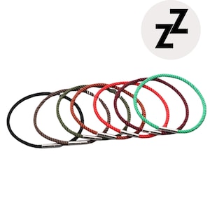 Może przedstawiać: Kolekcja siedmiu kolorowych bransoletek z liny. Bransoletki są w różnych kolorach, w tym czarnym, brązowym, oliwkowym, czerwonym, bordowym i zielonym. Każda bransoletka ma srebrne zapięcie i okrągły kształt. Białe koło z czarną literą "Z" znajduje się w prawym górnym rogu.