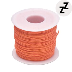 May include: A spool of orange thread, tightly wound around a white plastic core. The thread is a vibrant, solid color. A small, black and white logo with the letter "Z" is in the upper right corner.