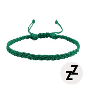 以下が含まれることがあります： 調節可能な紐が付いた、緑色の編み込みブレスレット。ブレスレットは織り込まれた素材で作られており、シンプルなデザインです。右下隅には、黒い文字「ZZ」が入った白い円があります。