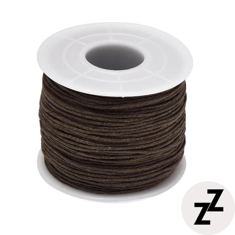 May include: A spool of dark brown waxed cord. The cord is tightly wound around a white plastic spool. The spool has a central hole and a circular base. The cord appears to be made of a durable material, suitable for various crafting projects.