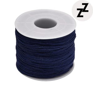 May include: A spool of dark blue waxed cord. The cord is tightly wound around a white plastic spool. The spool has a central hole and a circular design. A white circle with the letter "Z" is in the upper right corner.