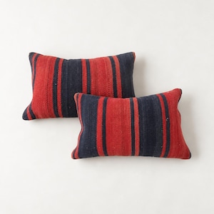May include: Two rectangular throw pillows featuring a woven pattern of vertical stripes in deep navy blue and vibrant red. The fabric has a textured appearance with consistent color distribution across both cushions, which are arranged slightly offset.