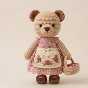 May include: A crocheted teddy bear wearing a pink dress with a white apron adorned with pink roses. The bear has brown eyes, ears, and shoes, and carries a small basket. A charming handmade toy.