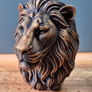 Könnte beinhalten: Eine detaillierte Skulptur eines Löwenkopfes mit einem Bronze- und Schwarzfarbschema. Die Mähne und die Gesichtszüge sind aufwendig geschnitzt und zeigen eine königliche und kraftvolle Ästhetik. Die Skulptur ist wahrscheinlich ein dekorativer Gegenstand.