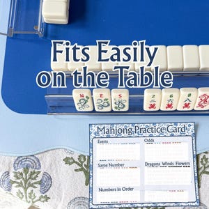 以下が含まれることがあります： 白い牌と青いゲーム盤を備えた麻雀セット。「Fits Easily on the Table」の文字が表示されています。練習カードも表示されており、偶数、奇数、その他のゲーム要素のセクションがあります。