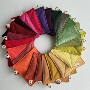 May include: A vibrant display of square quilted pot holders in a circular pattern. The pot holders showcase a spectrum of colours, from deep reds and oranges to verdant greens and sunny yellows. Each has a diamond quilt design and a hanging loop.